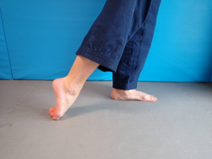 Fußoberseite dehnen: Stehe auf einem Bein und lege den Fuß des anderen Beins so nach hinten am Boden ab, dass die Zehenoberseite am Boden aufliegt. Halte den Körper aufrecht und verlagere das Gewicht auf das Standbein. Du solltest nun die Dehnung in der Fußoberseite spüren. Dauer: 1 Min / Fuß (Kürzer, wenn diese Dauer für dich noch zu viel ist und wenn der Fuß verkrampft).