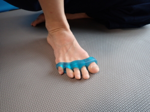 Zehen spreizen - passiv: Platziere den nackten Fuß so, dass du die Sohle mit der Hand gut erreichen kannst, z.B. indem du den Fuß sitzend am Knie des anderen Bein ablegst. Fahre nun mit den Fingern sanft in die Zehenzwischenräume und spreize die Zehen auseinander (links). Alternativ können auch Zehentrenner verwendet werden. Dauer: 1-2 Min / Fuß.